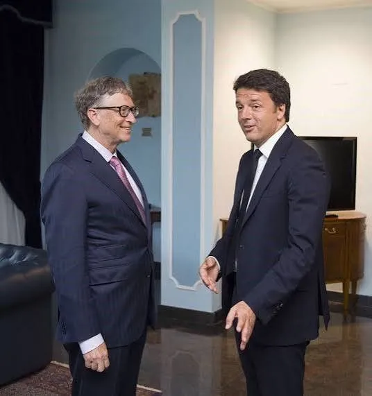 Zwei Männer im Anzug stehen in einem eleganten Innenraum und unterhalten sich. Links ist Bill Gates mit Brille und Krawatte zu sehen, rechts der italienische Politiker Matteo Renzi in dunklem Anzug. Beide stehen sich gegenüber und blicken einander an.
